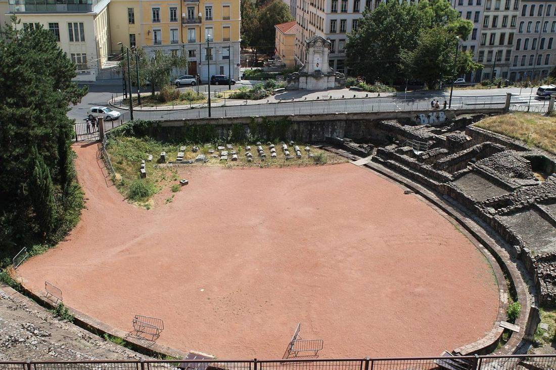 L'arène de l'amphithéâtre des Trois Gaules à Lyon vue depuis la rue Lucien Sportisse, avec les murs de soutènement des gradins et la grille au premier plan