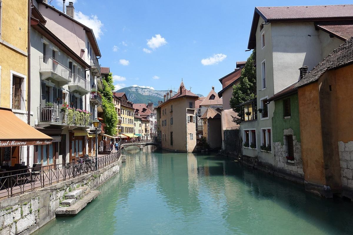 Le canal du Thiou dans la vieille ville d'Annecy, avec ses façades colorées, ses terrasses et le Palais de l'Île au fond
