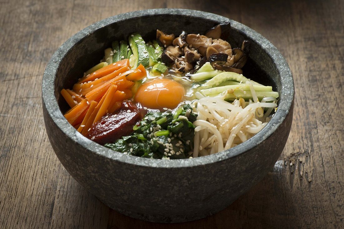 Un dolsot bibimbap servi dans son bol de pierre brûlant, avec riz, légumes assaisonnés disposés en secteurs et œuf au centre