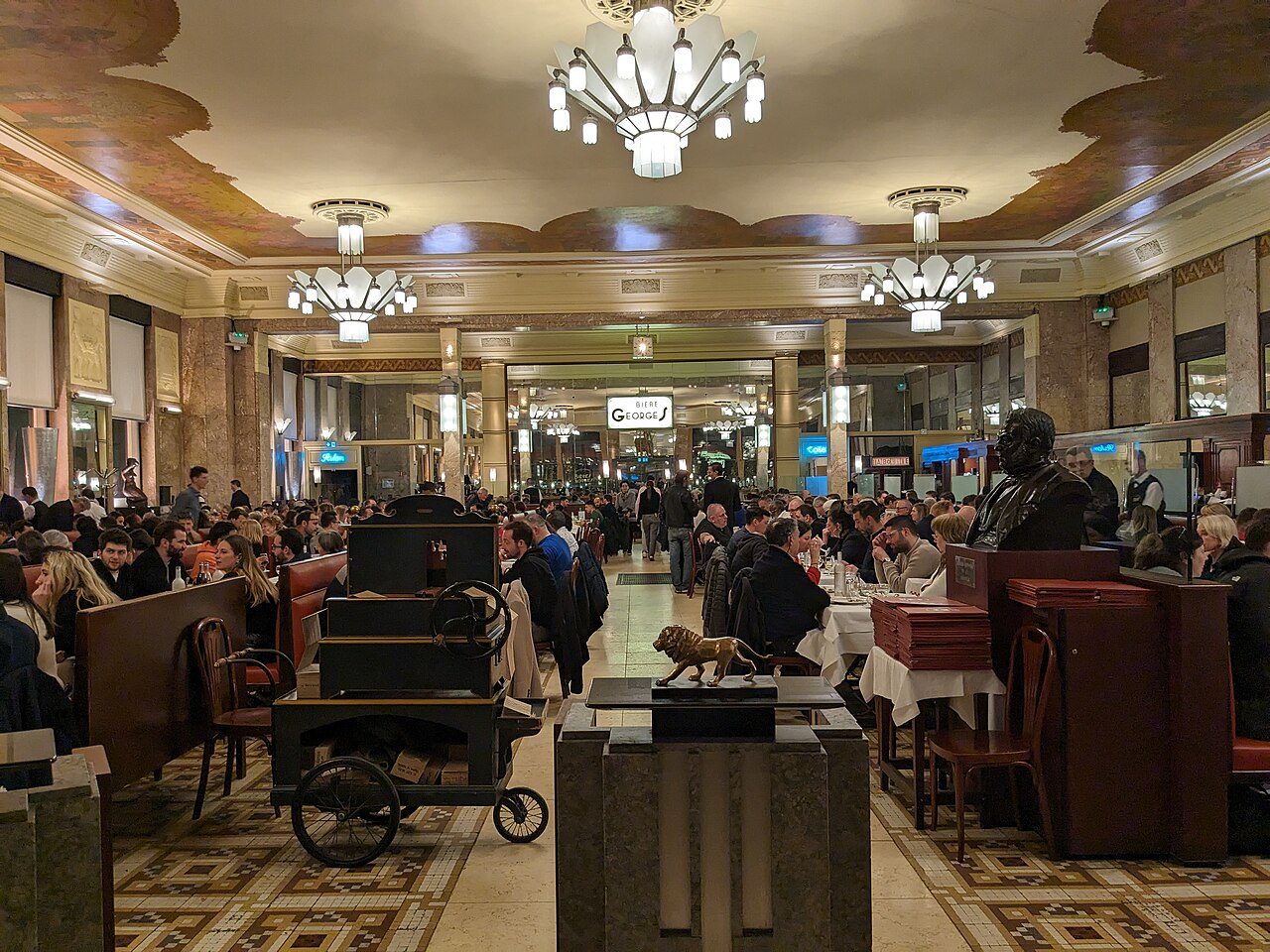 La grande salle de la Brasserie Georges, ses banquettes, ses lustres Art déco et son plafond peint, vue depuis l'entrée