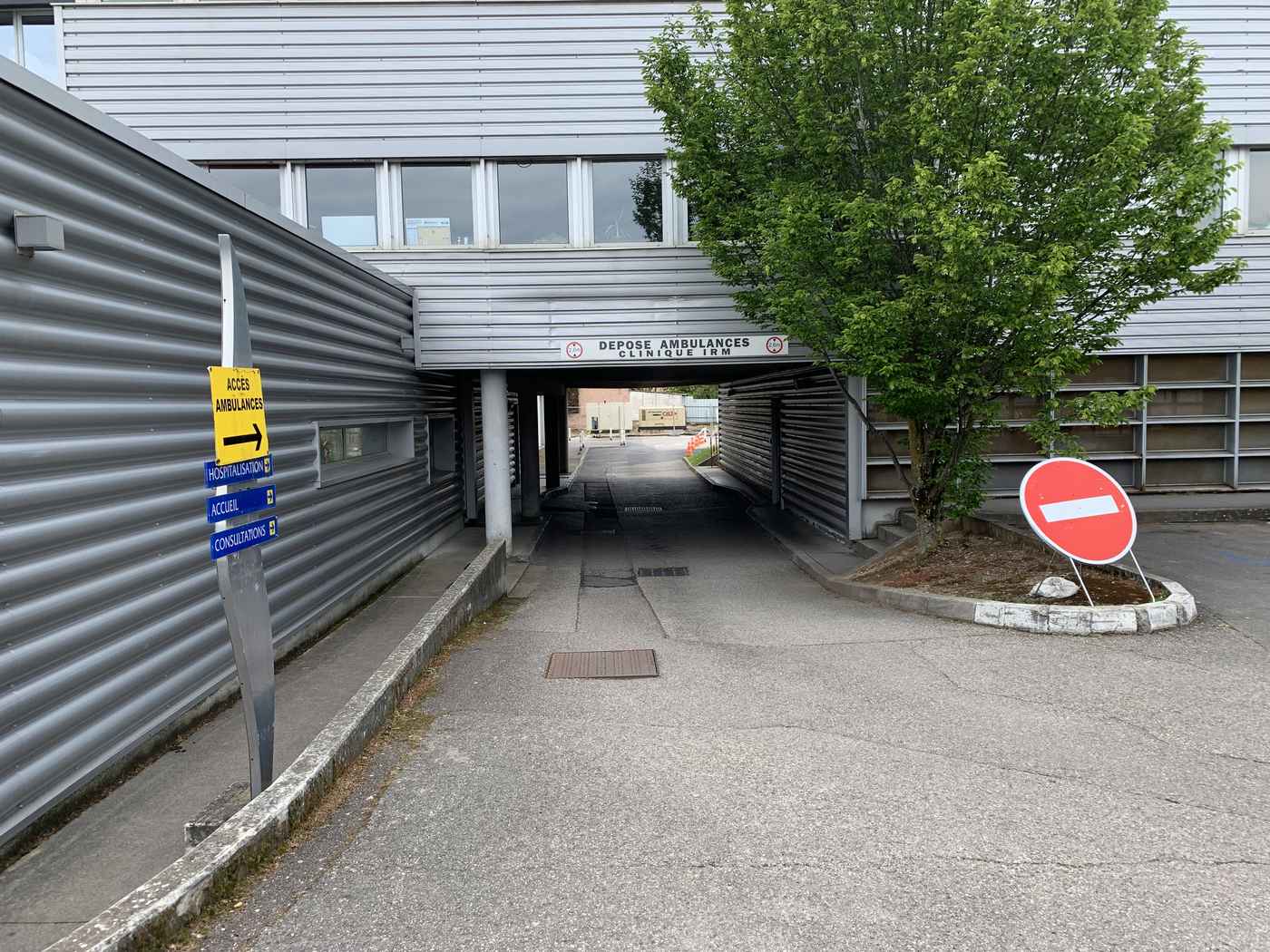 Voie de dépose des ambulances de la clinique Lyon-Nord à Rillieux-la-Pape, passant sous un bâtiment, avec le panneau de direction vers l'hospitalisation, l'accueil et les consultations