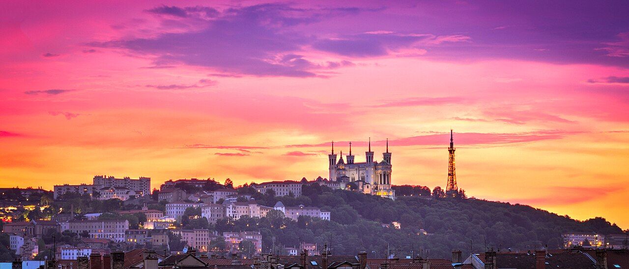 La basilique de Fourvière et la tour métallique sous un ciel rose et orange au coucher du soleil