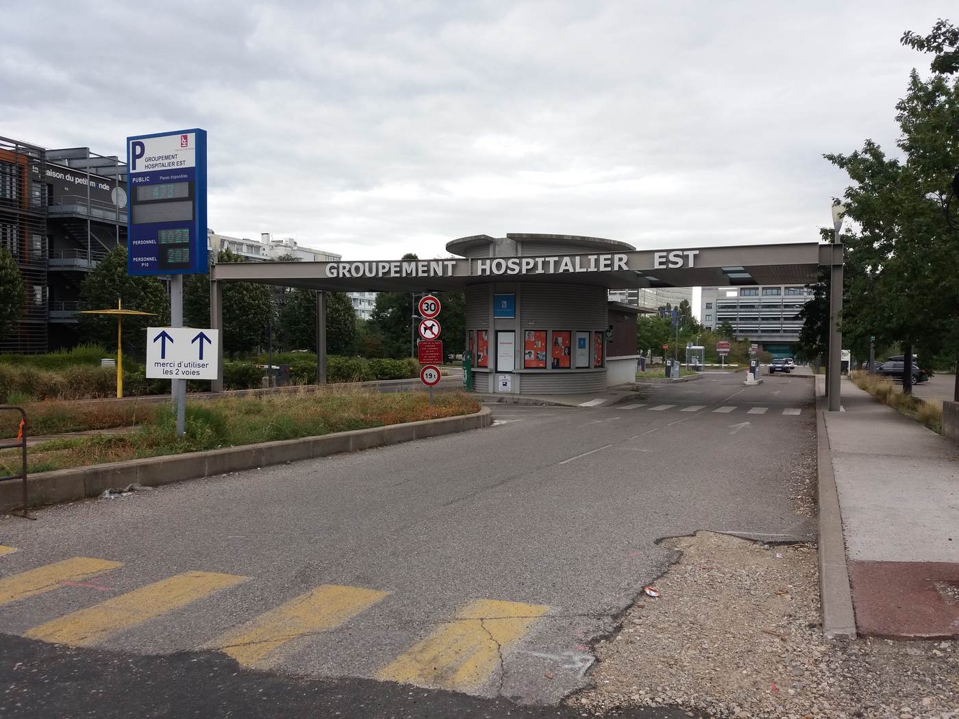 Portique d'entrée du Groupement Hospitalier Est, boulevard Pinel à Bron, avec la borne d'accueil et l'affichage des places de parking disponibles