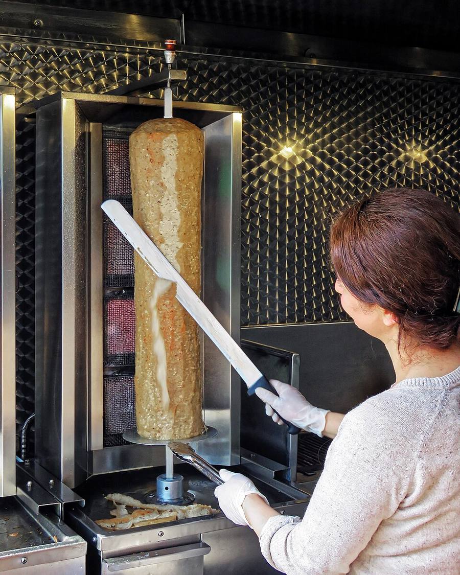 Une commerçante tranche au couteau la viande d'une broche verticale de kebab à l'agneau, dans son échoppe