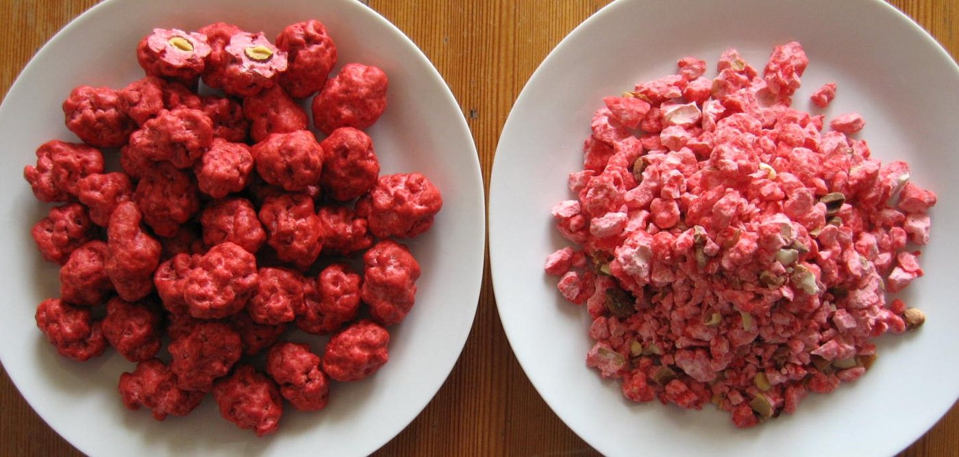 Pralines roses entières et concassées, montrant l'amande enrobée de sucre cuit rouge