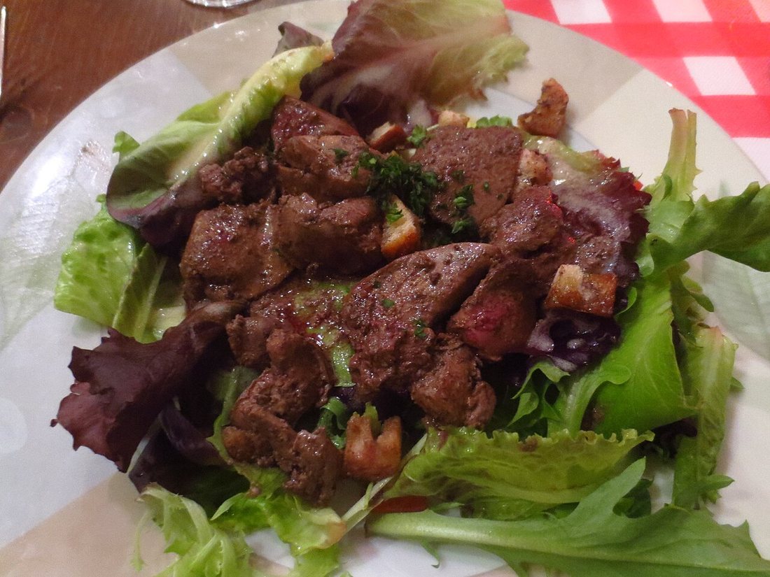 Salade lyonnaise servie avec des foies de volaille, de la frisée et un œuf poché