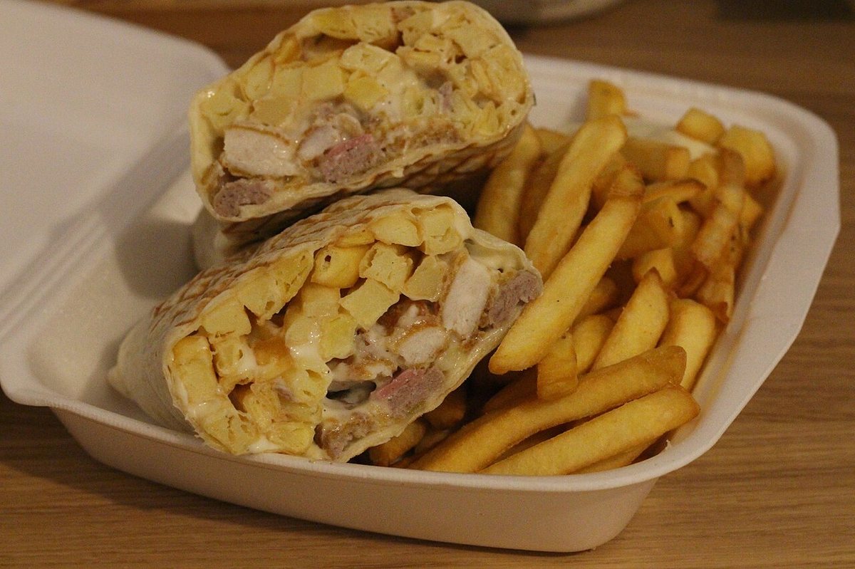 Un french tacos coupé en deux, laissant voir la viande, les frites et la sauce fromagère à l'intérieur de la galette pressée